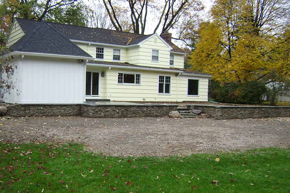 back of house with stone wall and driveway